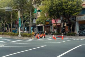 Workers painting road lanes in a bustling city intersection.